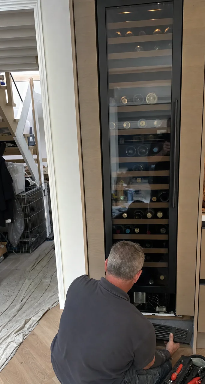A built-in column standing flush with a cabinet run, door closed, the interior light picking out the shelves.