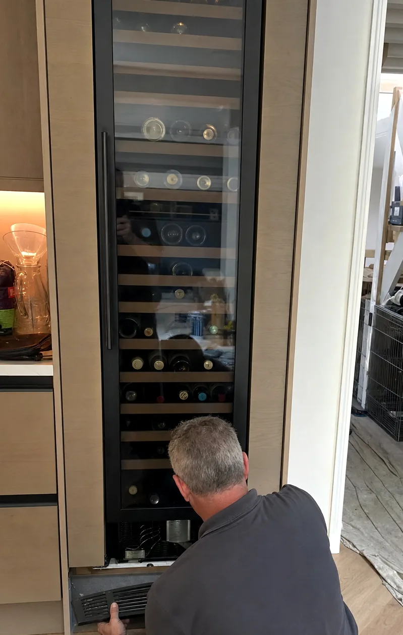 The base of a built-in column with the grille in a technician’s hand, cabinetry tight to both sides of the unit.