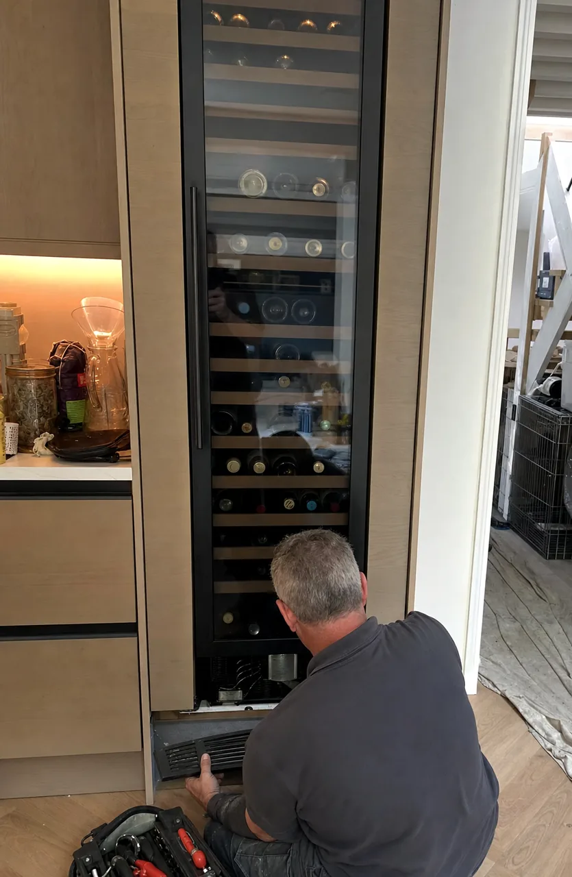 A full-height wine column built into cabinetry in a coastal kitchen, bottles lit on their racks behind the glass.